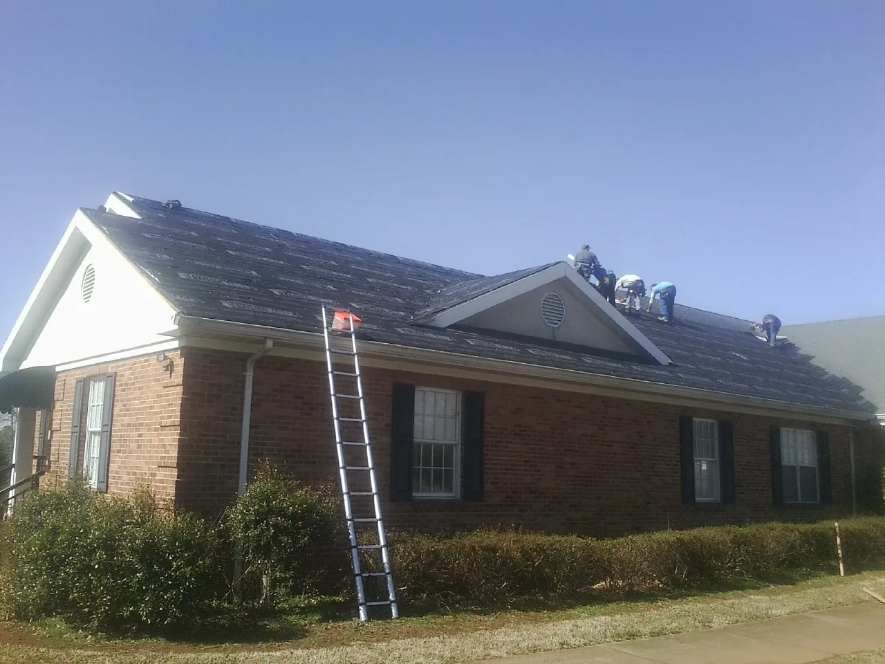 Crew tearing shingles off a brick ranch roof with a ladder set — Metal Roof Repair work by our crew in Parma