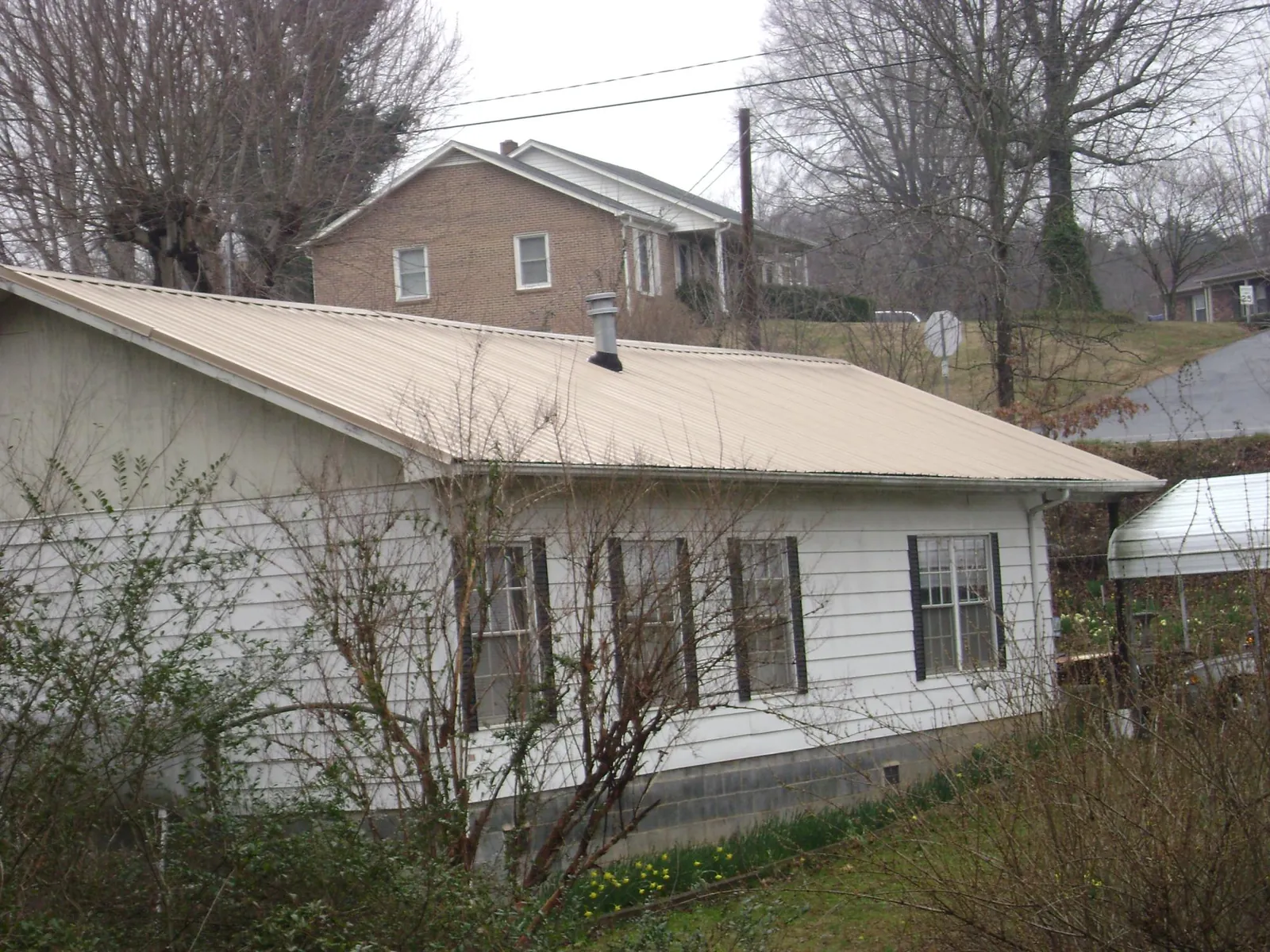 Tan metal roof on a white sided house set into a hillside — Commercial Roofing by Roofing Brothers in Parma